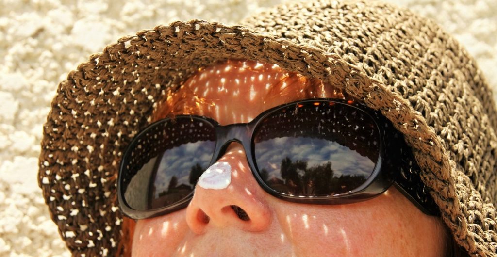 Woman with hat, sunglasses, and sunscreen on her nose.