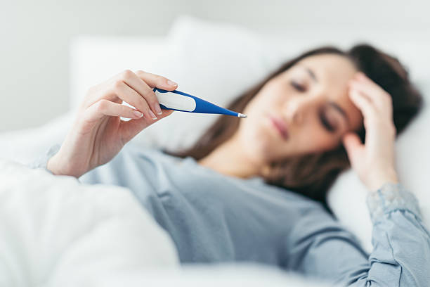 Woman looking at thermometer, laying in bed sick.